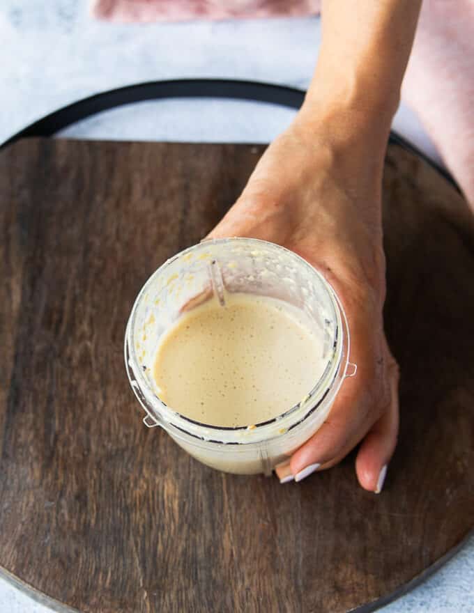Sesame salad dressing ready in a bowl of a food processor, A hand showing close up of how smooth it is