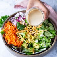 A hand pouring the sesame dressing over a bowl with the salad ingredients