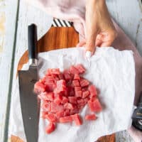 A hand chopping the fresh tuna into half an inch size cubes on a cutting board