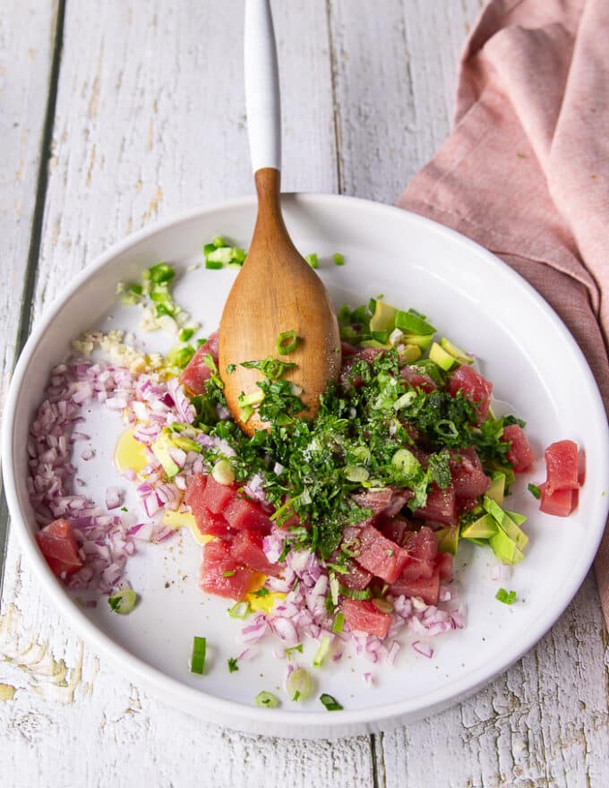 All the ingredients for the tuna ceviche are added into a shallow plate: diced avocados , jalapenos, green onions, red onions, cilantro, lime juice, garlic, olive oil
