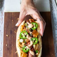 An assembled Hawaiian style hot dog showing the grilled hot dog with spicy slaw, jalapenos and grilled pineapples