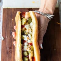 An assembled classic grilled hot dog showing the grilled hot dog with mustard, ketchup, relish or cornichons pickles, diced onions