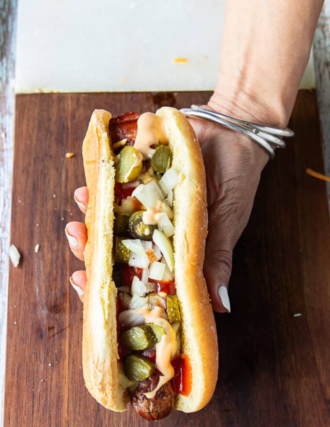 An assembled classic grilled hot dog showing the grilled hot dog with mustard, ketchup, relish or cornichons pickles, diced onions 