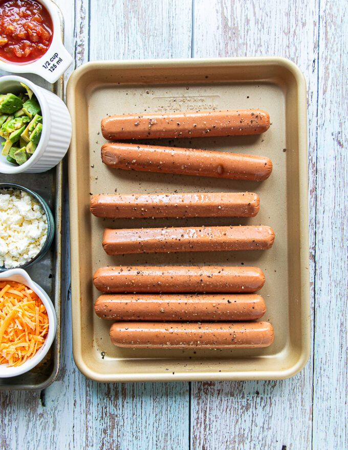 Seasoned hot dogs with salt and pepper and oil in a sheet pan 