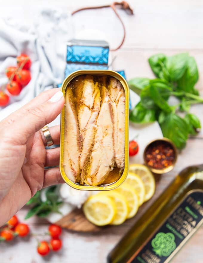 A hand holding an opened can of sardines showing the boneless skinless sardines in a can