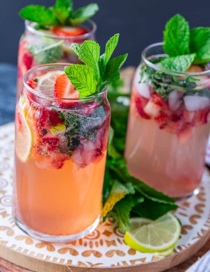 Close up on one strawberry mojito showing the crushed strawberries, lime slices and mint and garnished with more berries, mint and lime 