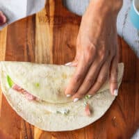 detailed step by step on how to fold a tuna wrap starting by showing folding the one side of tortilla over the filling