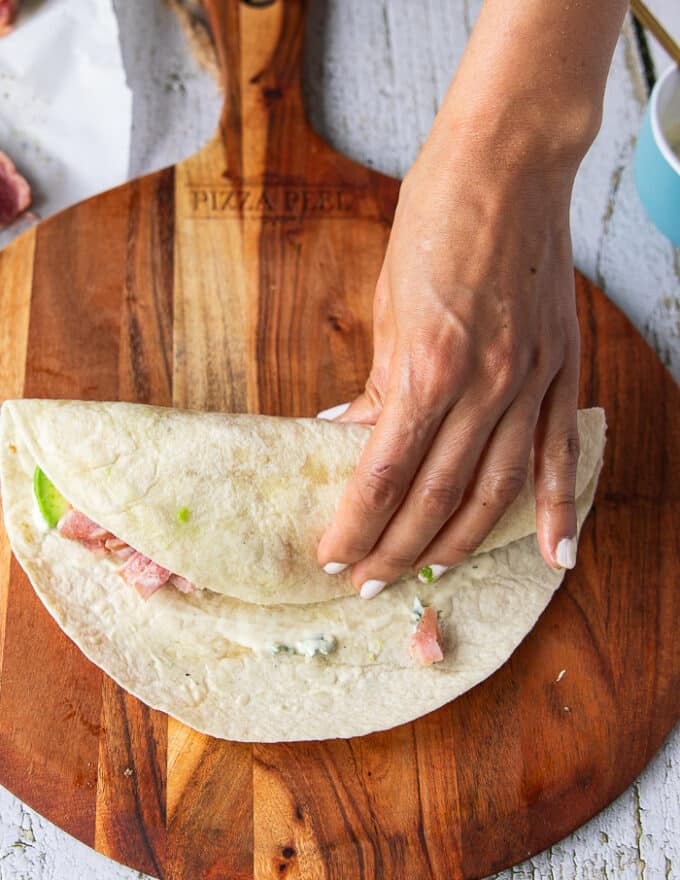 detailed step by step on how to fold a tuna wrap starting by showing folding the one side of tortilla over the filling 