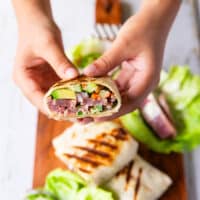 A hand holding a cut up tuna wrap showing the tuna filling with the avocado, onions and more close up