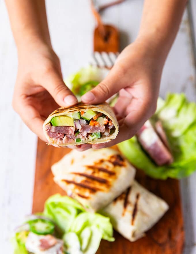 A hand holding a cut up tuna wrap showing the tuna filling with the avocado, onions and more close up