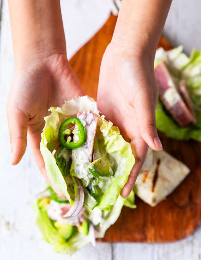 A hand holding a lettuce with the tuna, veggies and sauce drizzled on top.